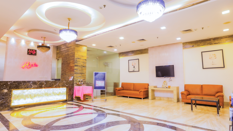 Hotel lobby area with a reception desk, sofas, and wall-mounted TV at Hyphen Premier Hotel, Meerut.