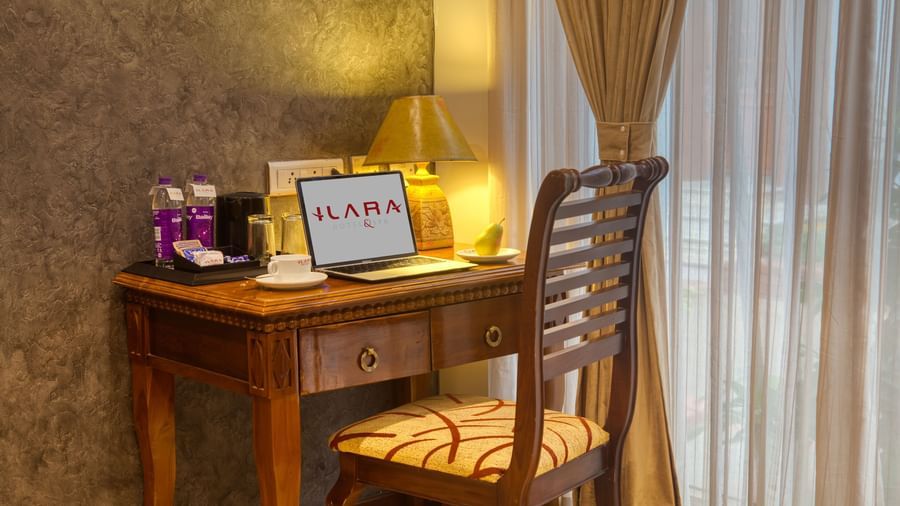 Dedicated wooden work desk with welcome kit and tea setup near a sheer curtain at Ilara Hotels & Spa, OMR, Chennai