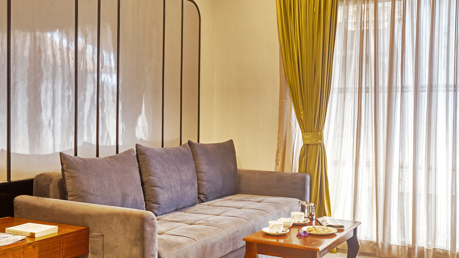 Living room with grey sofa, sheer curtains, and coffee table in a well-lit space at Ilara Hotels & Spa, OMR, Chennai