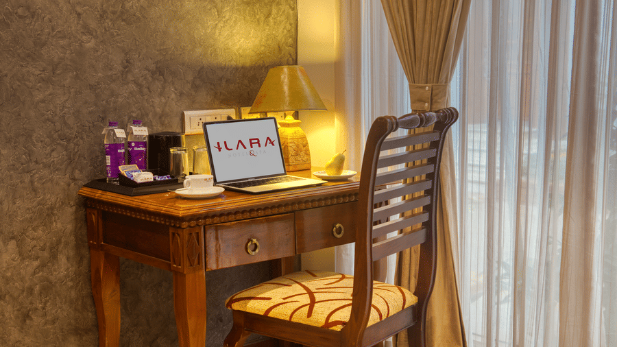 Dedicated wooden work desk with welcome kit and tea setup near a sheer curtain at Ilara Hotels & Spa, OMR, Chennai