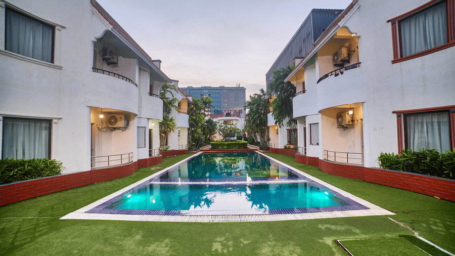 A symmetrical view of Ilara Hotels & Spa, OMR, Chennai with red roofs, flanking a long, narrow swimming pool or water feature, bathed in daylight.