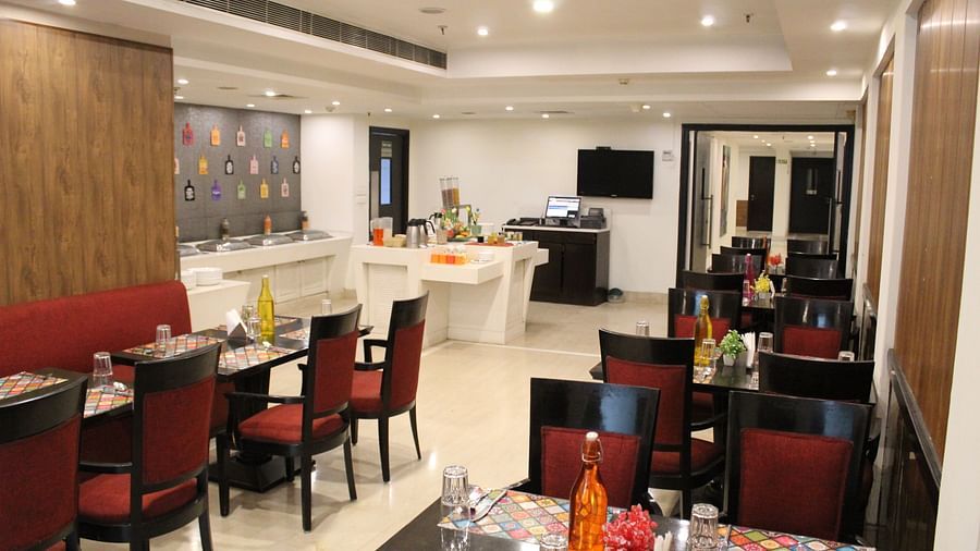 An image of a restaurant several sets of chairs and table where plates, cutlery, napkin, water bottles and other items are kept - Inde Hotels Vista Woods