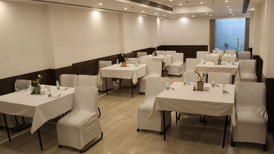 An image of a banquet hall at Inde Hotels Vista Woods featuring several sets of chairs and table where water bottles and flower pots are placed 