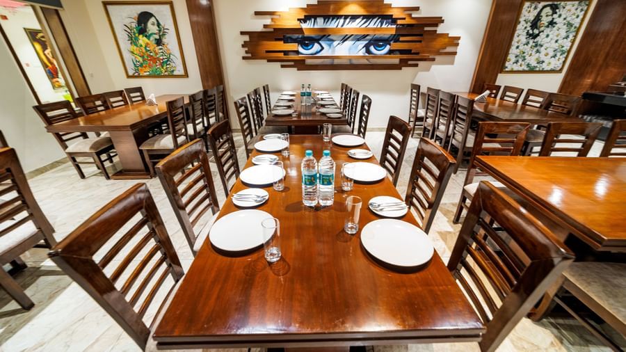 Dining area at Inde Reva Resorts Rishikesh with a long wooden table, cushioned chairs, framed artwork, and a neatly arranged dining setup.