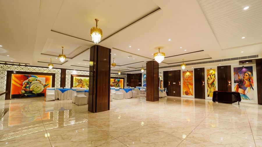 Banquet hall at Inde Reva Resorts Rishhikesh with marble flooring, ceiling lights, and artwork displayed along the walls.