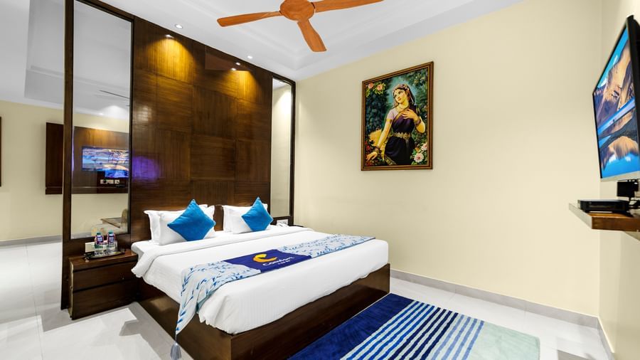 Bedroom at Inde Reva Resorts Rishhikesh with a double bed, blue cushions, ceiling fan, TV, and framed artwork on the wall.