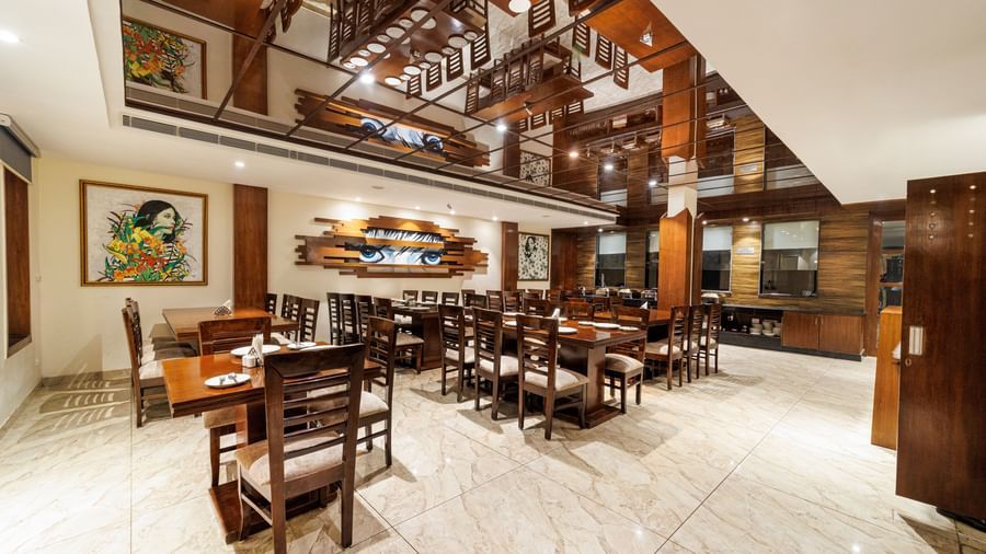 Restaurant at Inde Reva Resorts Rishhikesh featuring wooden furniture, open ceiling design, framed art, and tiled flooring.