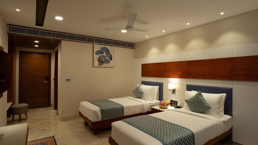 Deluxe Room with twin beds along with a wooden side table with a lamp and wooden table and chair at Inde Signature Jaipur