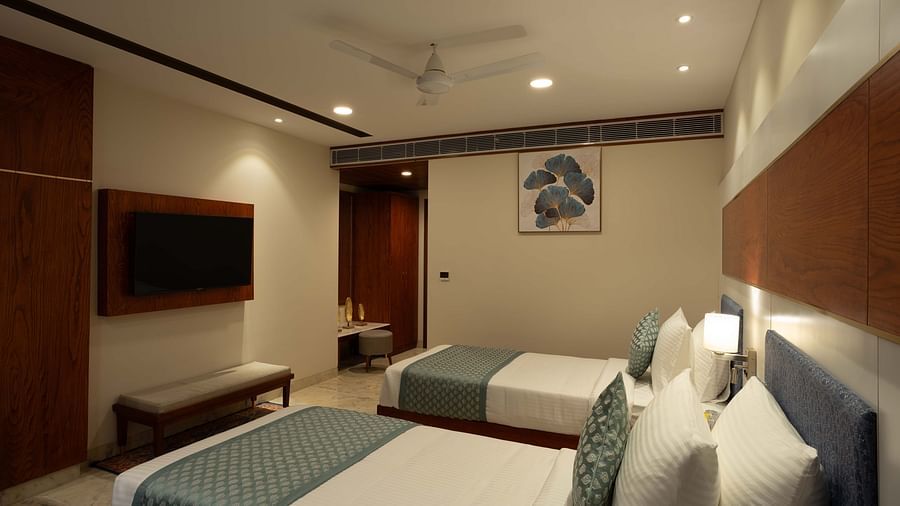 Deluxe Room with twin beds along with a wooden side table with a lamp, wooden table and chair, and wall mounted television at Inde Signature Jaipur