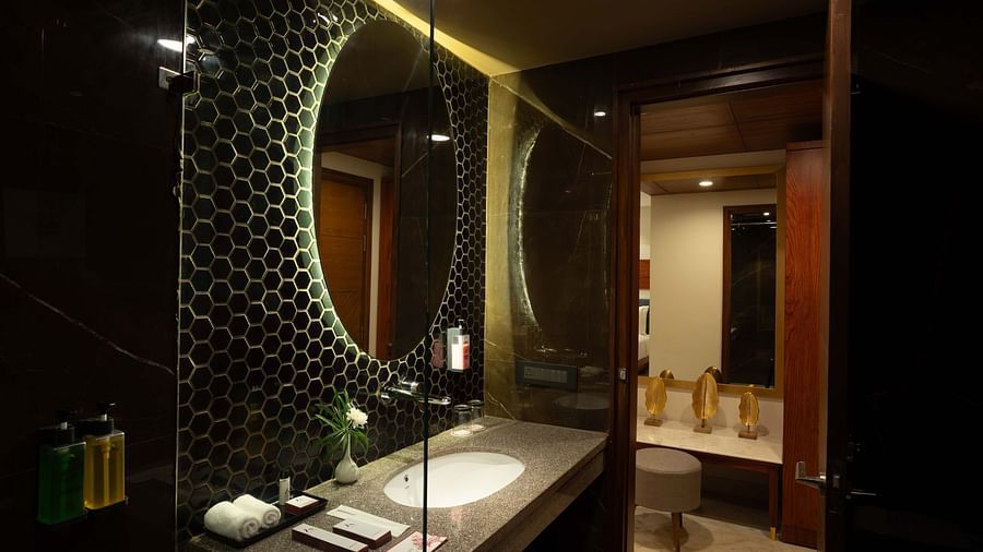 Round shaped mirror above the washbasin with transparent glass divider separating the showering and toilet areas in the Deluxe room's bathroom at Inde Signature Jaipur.