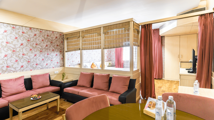 A lounge area with sofas, red chairs, wallpapered wall and wooden table at Infiniti Hotel, Indore.