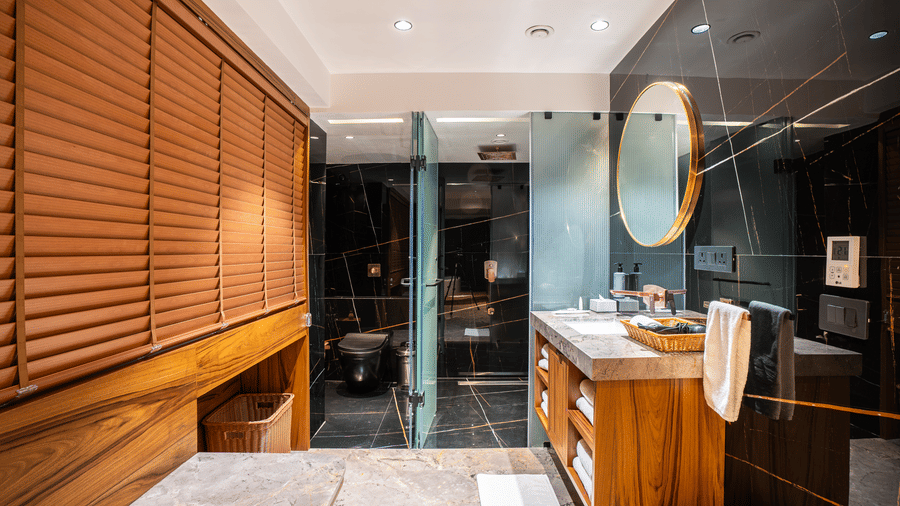 A bathroom with a wall mounted mirror, washbasin and glass shower partition at Infiniti Hotel, Indore.