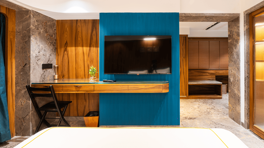 A bedroom with a television mounted on a teal wall and wooden furniture at Infiniti Hotel, Indore.