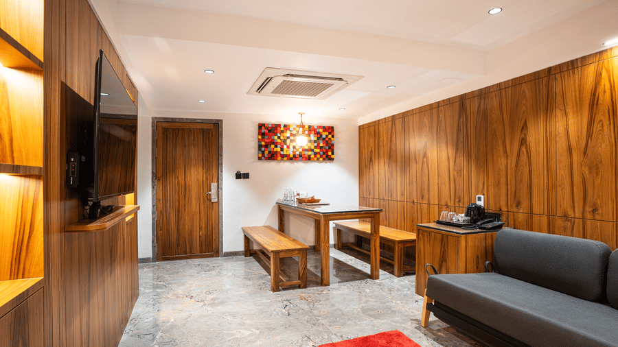 A suite with wooden walls, grey sofa, dining table, television and decorative painting at Infiniti Hotel, Indore.