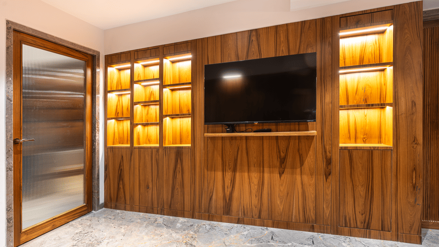 A room with wooden wall panelling, built-in television and illuminated shelves at Infiniti Hotel, Indore.