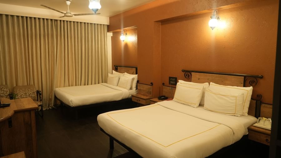 Bedroom with two double beds, curtains and warm lighting at Infiniti Hotel, Indore.