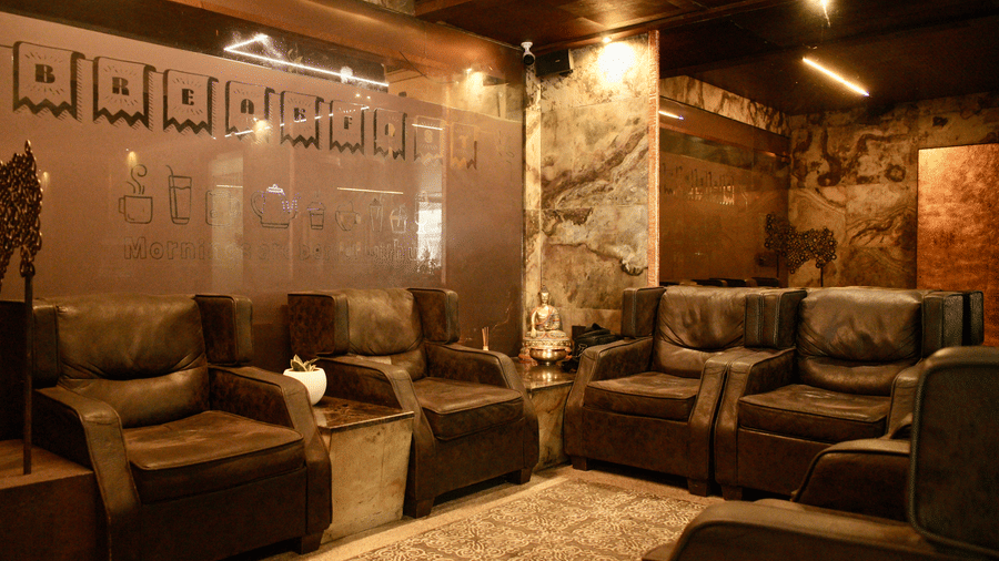 A seating area at Infiniti Hotel, Indore featuring 5 leather armchairs, side tables, and decorative wall panels.