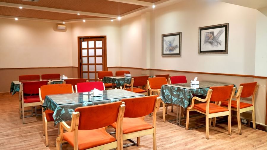 A close-up view of the empty dining area with set tables and a wooden door visible in the background at Infiniti Hotel, Indore.