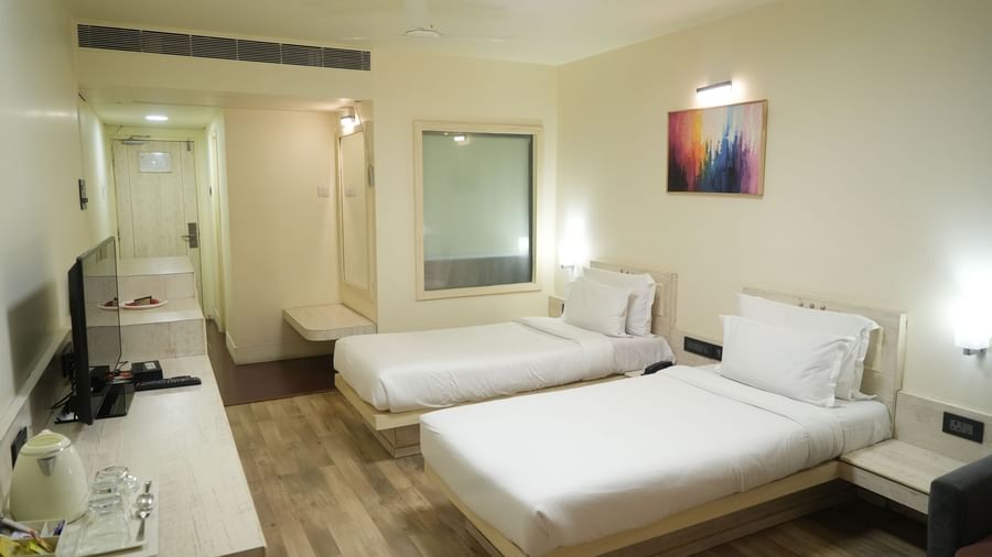 Bedroom with 2 single beds, a television, desk and wall paintings at Infiniti Hotel, Indore.