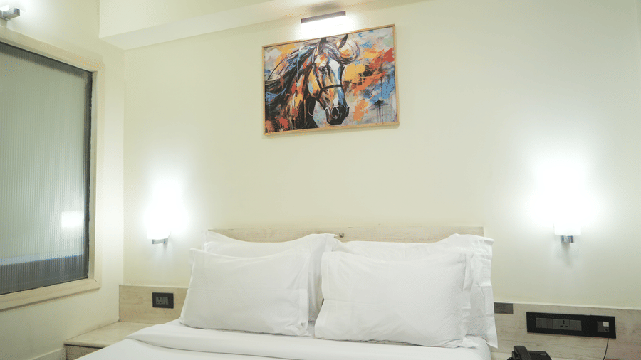 A bedroom at Infiniti Hotel, Indore featuring double bed, wall lamps, artwork, and bedside tables.  