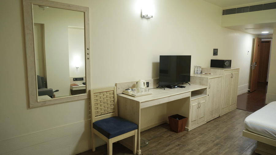 A bedroom at Infiniti Hotel, Indore featuring study desk, chair, mirror, television, and safe box.