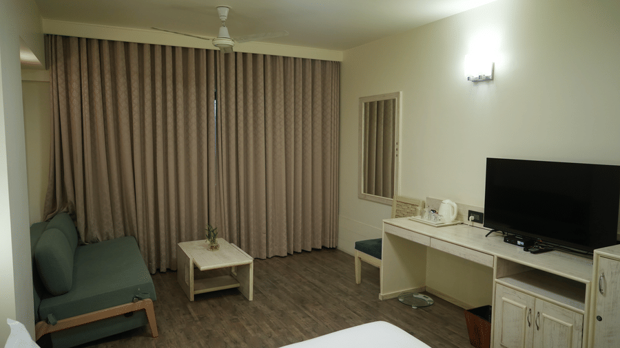 A bedroom at Infiniti Hotel, Indore featuring double bed, sofa, coffee table, and television unit.  