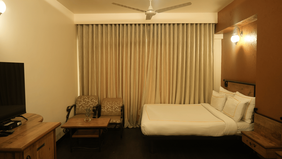A bedroom at Infiniti Hotel, Indore featuring double bed, armchairs, coffee table, and television cabinet.