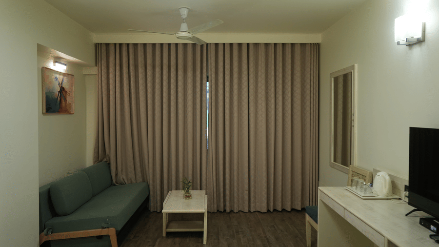 A bedroom at Infiniti Hotel, Indore featuring sofa, coffee table, full length curtains, and television unit.