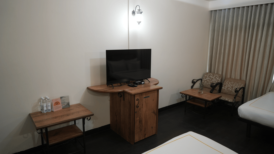 A bedroom at Infiniti Hotel, Indore featuring television unit, chairs, coffee table, and side desk.