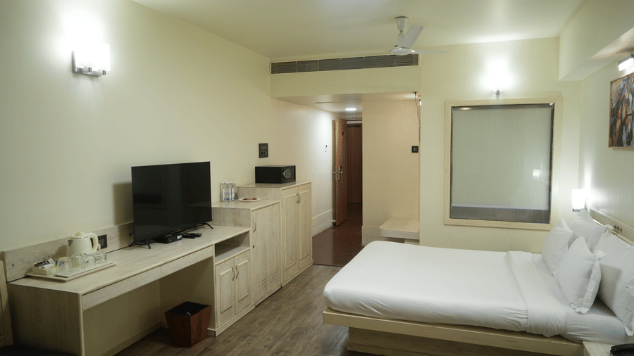 A bedroom at Infiniti Hotel, Indore featuring double bed, television console, study desk, and safe box.  