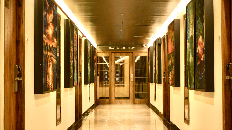A corridor at Infiniti Hotel, Indore featuring framed artwork, mirror, and glass door at the end.