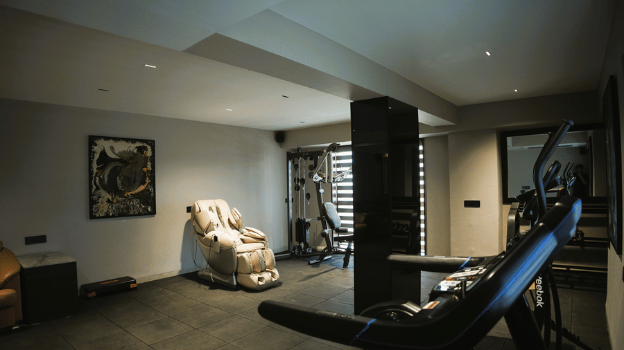 A fitness centre at Infiniti Hotel, Indore featuring exercise equipment, massage chair, and artwork on the wall.
