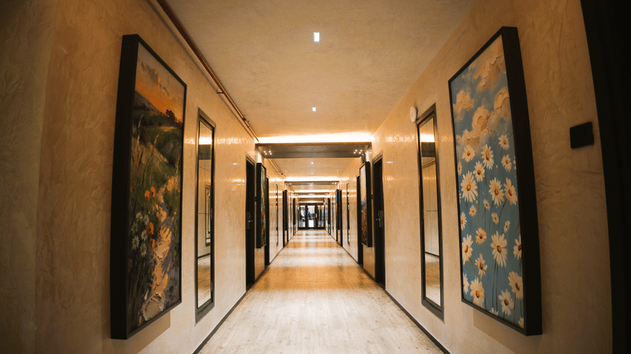 A long corridor at Infiniti Hotel, Indore featuring wall artwork, mirrors, and wooden guest room doors.