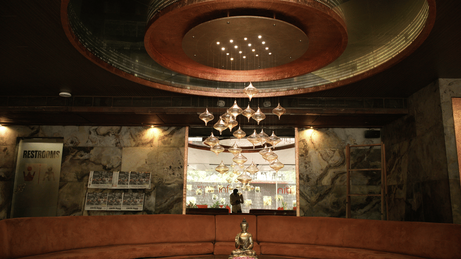 A lounge area at Infiniti Hotel, Indore featuring curved seating, central table with statuette, and hanging lights.
