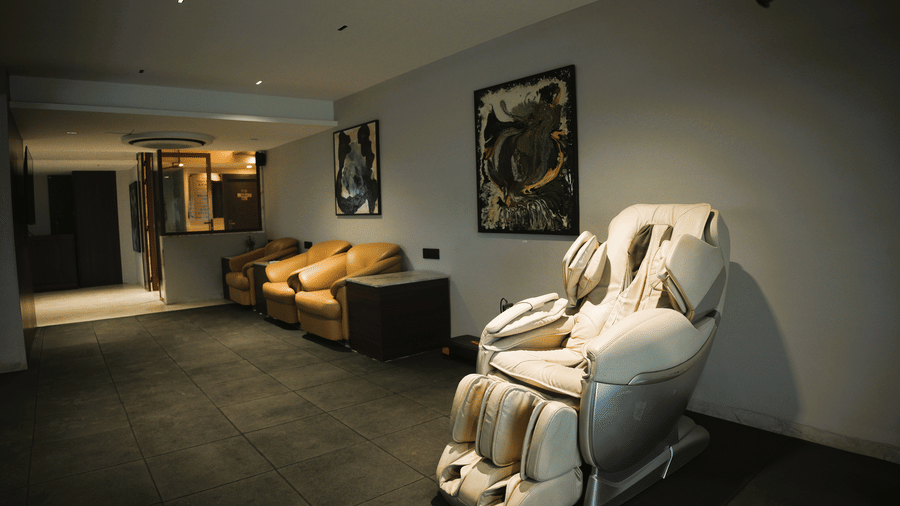 A relaxation area at Infiniti Hotel, Indore featuring massage chair, armchairs, and framed art on the wall.