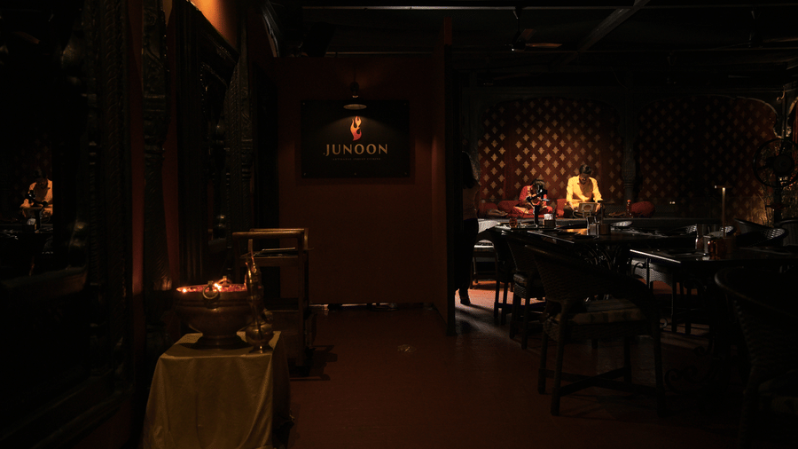 Infiniti Hotel, Indore | A dining space with a sign board, lights and people sitting near a table.