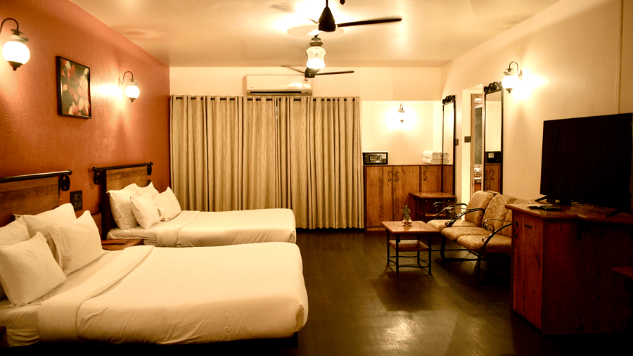 A bedroom at Infiniti Hotel, Indore featuring 3 double beds, sofa, coffee table, television unit, and full length curtains.  