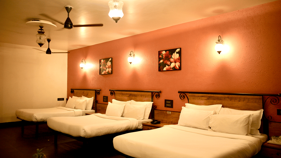 A bedroom at Infiniti Hotel, Indore featuring 3 double beds, wall artwork, lights, and side tables.