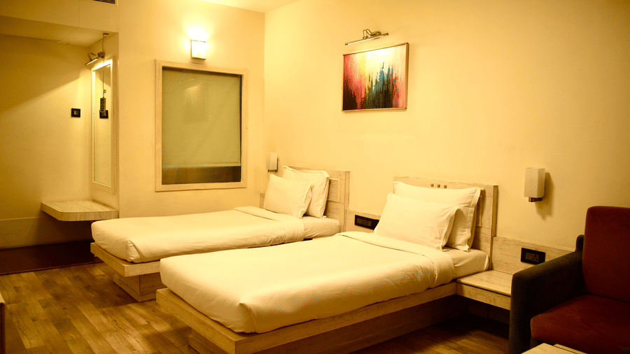 A bedroom at Infiniti Hotel, Indore featuring 2 single beds, sofa, coffee table, and wall art.
