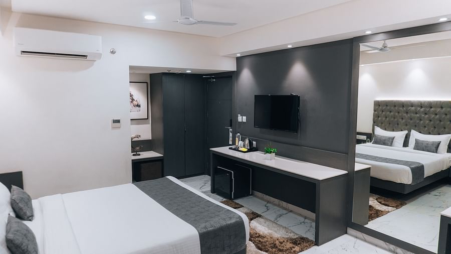 a bedroom with the bed facing a mounted television, with a workdesk beneath and a large mirror on the side - Jardin Hotels, Indore