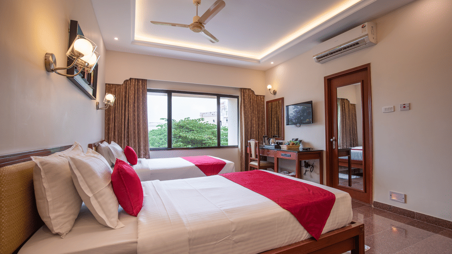 A modern Premium Room with twin beds, a large window with curtains, a ceiling fan, TV, desk, and wall-mounted lights