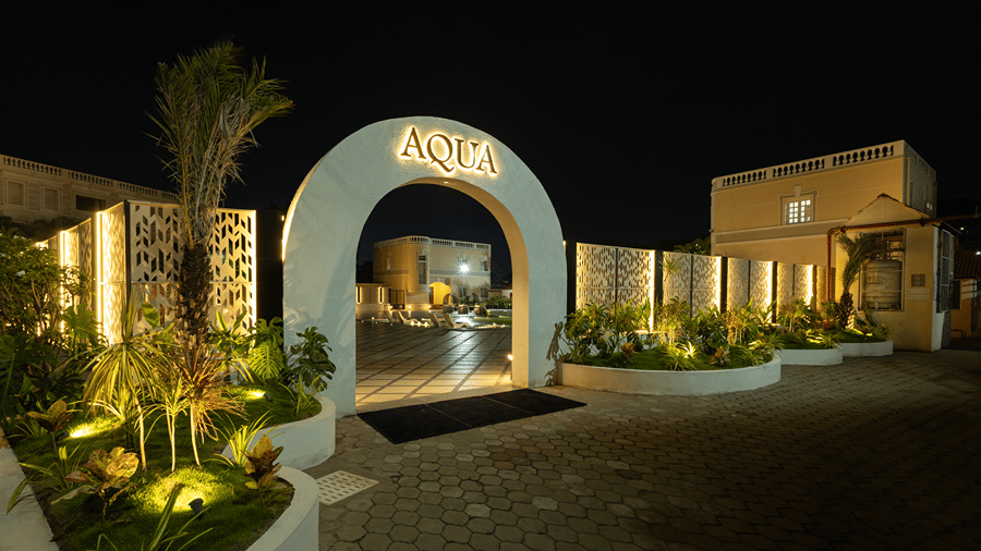 Front view of the illuminated arched entrance to the Aqua pool area surrounded by lush garden greenery at night at Jenneys Residency.