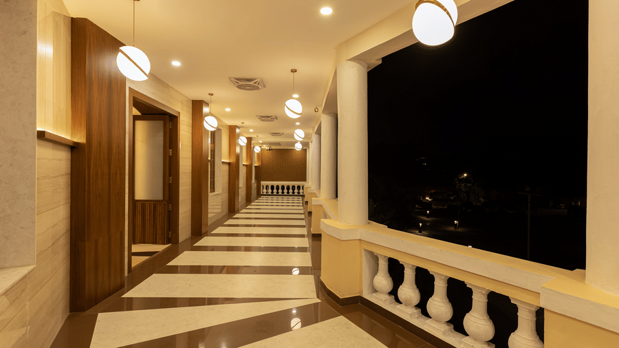 A brightly lit ballroom foyer leading to a balcony with white pillars and geometric floor tiling - Jenneys Residency, Coimbatore