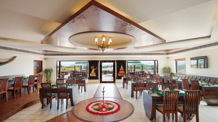 A wide view of a formal dining hall with traditional decor and large windows providing natural light - Jenneys Residency, Coimbatore