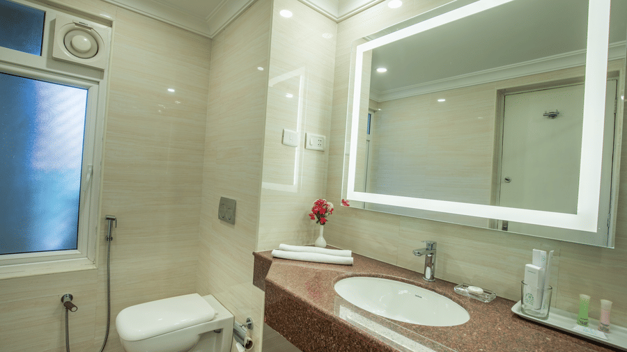 A clean and well-lit bathroom featuring a wall-mounted toilet and a large rectangular LED mirror - Jenneys Residency, Coimbatore