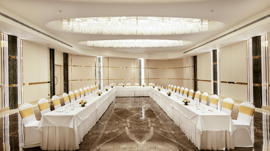 Emerald Hall set up in a U-shape arrangement with white linens and gold chairs at Jenney Residency, suited for meetings and events.