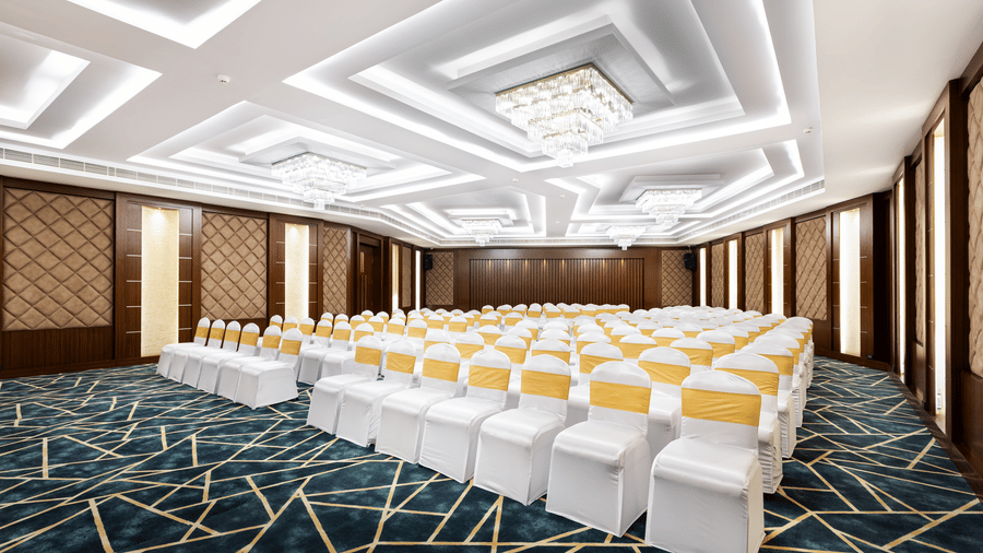 A hall at Jenneys Residency with chairs, chandeliers, and checkered floor.