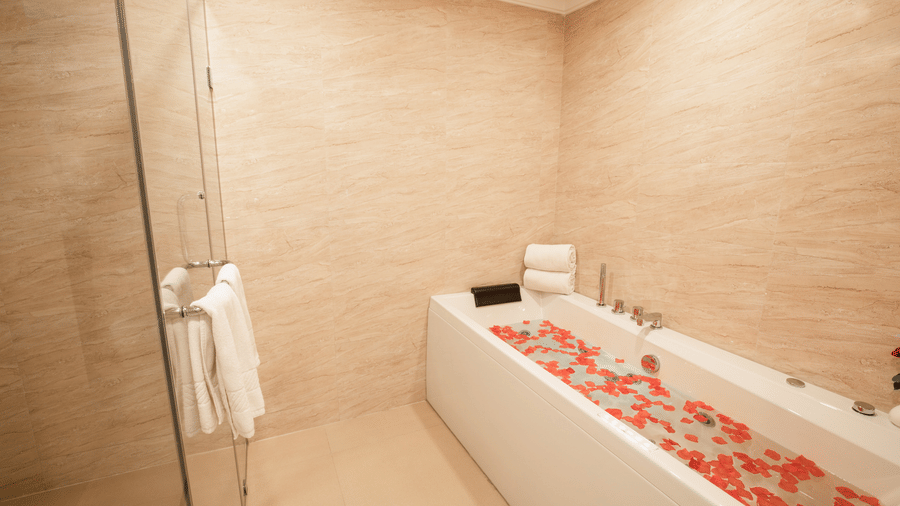 A high-angle shot of a modern white bathtub filled with water and floating red flower petals - Jenneys Residency, Coimbatore