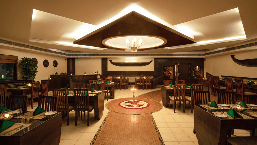 A symmetrical view of an indoor dining hall with dark wood tables and a geometric triangular ceiling design - Jenneys Residency, Coimbatore