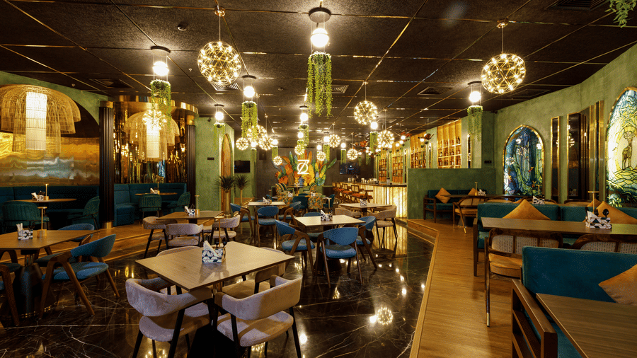 An upscale indoor restaurant featuring modern lighting fixtures wooden tables and teal upholstered chairs - Jenneys Residency, Coimbatore